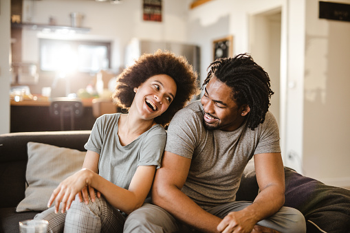 Cheerful black couple having fun while talking on sofa at home.
