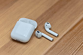 Mobile airpods on wooden blurred background. Apple wireless earphones with charger box, chosen focus.