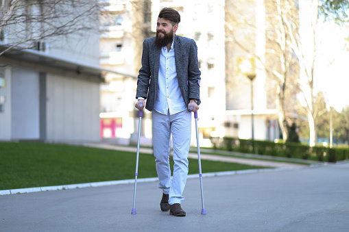 Young beautiful bearded man with walking sticks on the street, taking a stroll and enjoying sunny day. Outdoor environment