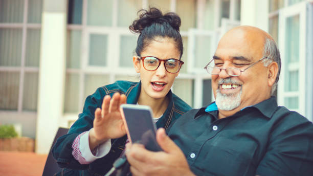 seniorenmann nimmt hilfe beim smartphone von einer jungen frau - senior adult with daughter father stock-fotos und bilder