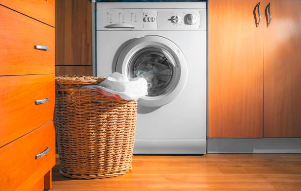 istock Large Wicker Laundry Basket, Lid Opened, Near the Front Load Washing Machine with Laundry. House Interior Laundry Room. Wood Interior Design. 1154767275