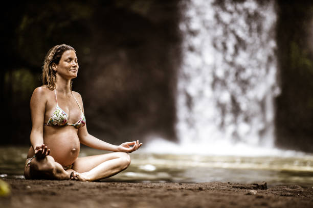 lächelnde schwangere frau meditiert in lotusposition am regenwald. - waterfall water nature zen like stock-fotos und bilder