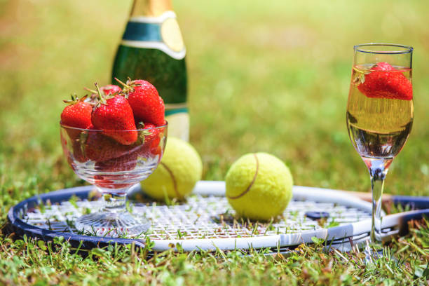 Tennis game. Strawberries, champagne and tennis balls with rackets on the green grass. Sport, recreation concept stock photo