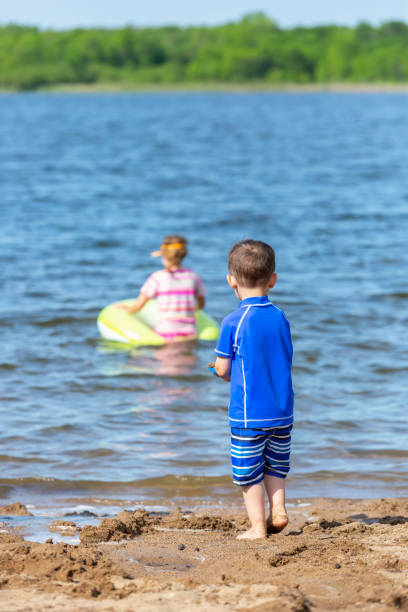 istock Young Boy At Beach Watching Sister In the Water 1154778093