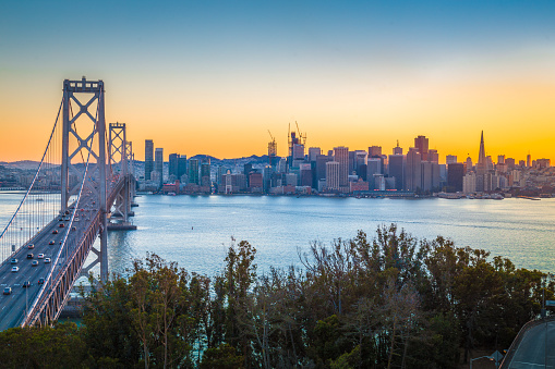 Classic panoramic view of famous Oakland Bay Bridge with the skyline of San Francisco illuminated in beautiful twilight with sunset glow in summer, California, USA