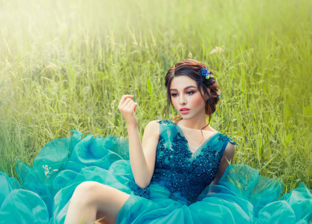 encantadora história misteriosa sobre boneca de porcelana, linda menina em longo azul exuberante vestido delicado. senhora com cabelo trançado escuro e make-up delicado, pele perfeita, flor na grama verde na natureza fresca - braided women sensuality portrait - fotografias e filmes do acervo