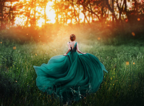 magical picture, girl with red hair runs into dark mysterious forest, lady in long elegant royal expensive emerald green turquoise dress with flying train, amazing transformation during fiery sunset - bride wedding fashion evening gown imagens e fotografias de stock