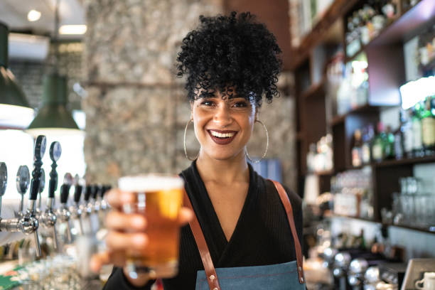 female bartender looking at camera and holding a beer - beer pub women pint glass imagens e fotografias de stock