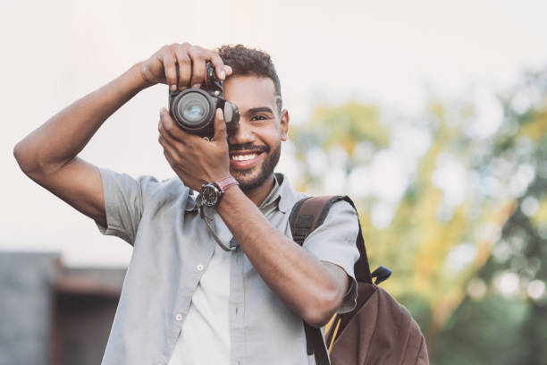 istock Young smiling man photographer with dslr camera in a city 1154794321