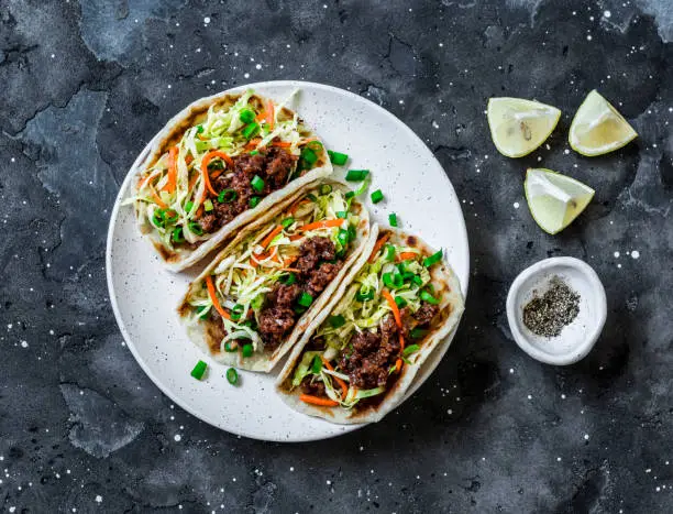 Photo of Spicy beef and cabbage, carrots pickled salad tacos on dark background, top view