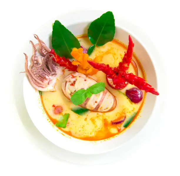 Tom yum pla muek Thaifood spicy soup with squid.Thai symbolic food Thaicuisine is national of Thailand decorated with chili carved top view isolated on white background