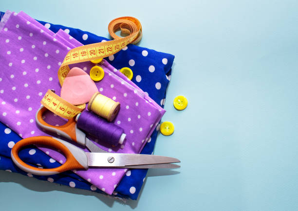 Sewing accessories and fabric on a blue background. Concept for needlework, stiching, embroidery. Sewing multicolored threads, needles, pins, fabric, buttons and sewing centimeter. top view, flatlay