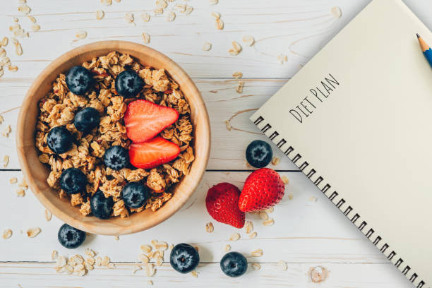istock Homemade granola and fresh berries on wood table with note book and text diet plan concept, copy space. 1154804865