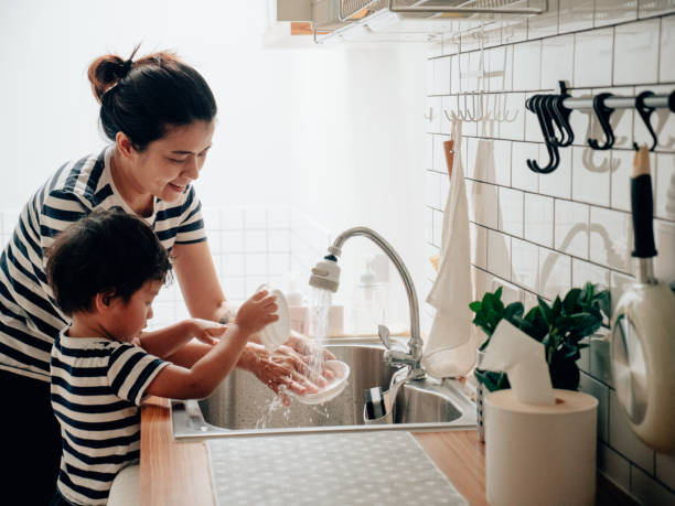 jeune femme nettoyant des plats avec son fils à la maison. - rubbing human hand togetherness women photos et images de collection