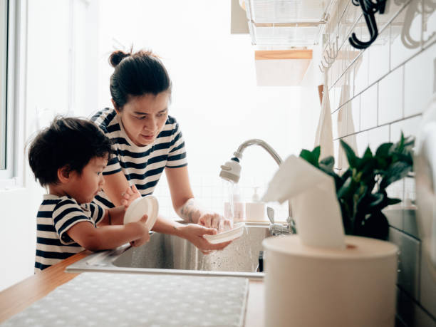 jeune femme nettoyant des plats avec son fils à la maison. - rubbing human hand togetherness women photos et images de collection