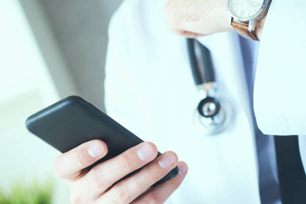istock Male doctor in white coat is using a modern smartphone device with touch screen. Doctor hands with mobile phone. 1154808622