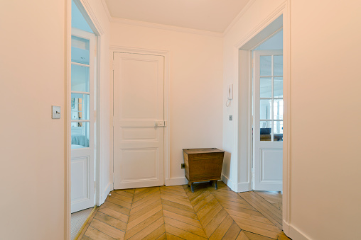 Room of an empty house with gloss oak parquet floors with black anodized aluminum window and aluminum radiator on the walls, white access door and carpentry of the same color