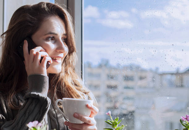 istock beautiful woman talking on smartphone at window 1154810722