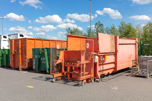 orange waste compactors are standing on a factory site with other waste containers next to them