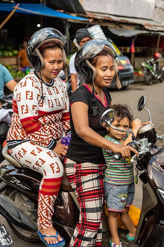 Makassar, Sulawesi, Indonesia - February 28, 2019: Terong Street Market. Closeup of three females on one scooter, all wearing pants. Street scene.
