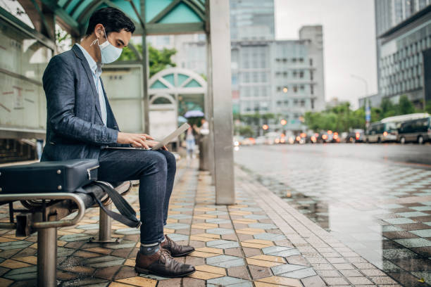 Businessman with flu mask using laptop on bus station