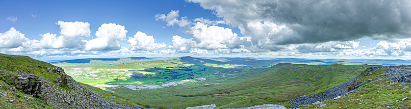A panoramic view of a mountain valley with grassy green slope under a majestic blue sky and white clouds