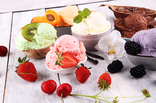 Set of ice cream scoops of different colors and flavours with berries, nuts and fruits decoration on white background