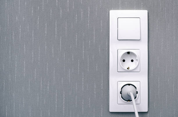 istock Light switch, power sockets, lead and plug on gray wall. 1154834238
