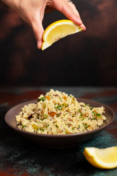 traditioneller couscous mit gemüse und kräutern in einer schüssel. zitrone in der hand. levantine vegetarischer salat. libanesische, arabische küche. nahaufnahme. senkrecht. - tabbouleh vegeterian food middle stock-fotos und bilder