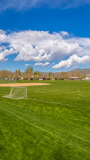 Panorama Soccer field and baseball field with view of mountain and cloudy blue sky. Houses and trees can also be seen around the perimeter of the sports field.