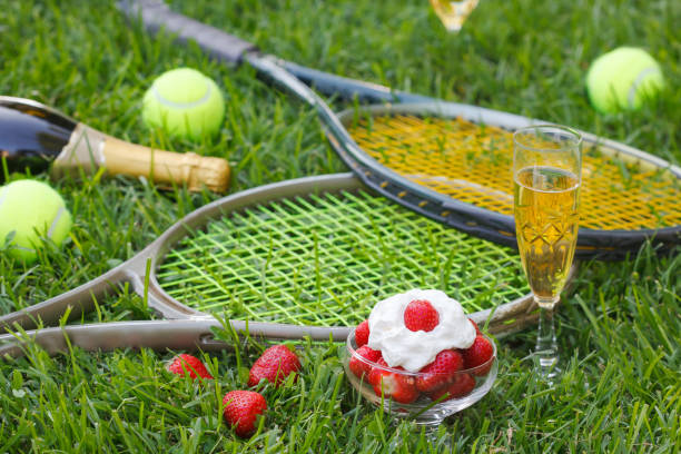 Strawberries with whipped cream, glass with champagne and tennis equipment on Wimbledon tournament grass stock photo