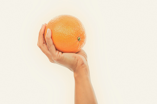 This is a clean simple image of a hand holding an orange with a lot of copy space. The image is styled in a warm retro tone to make it look vintage.
