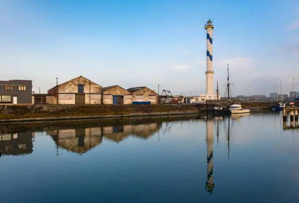 The famous lighthouse of Ostend city with a reflection in one of the commercial docks of the harbor, West Flanders, Belgium.