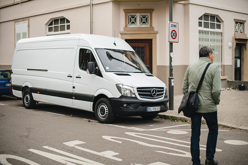 Strasbourg, France - Apr 5, 2017: Adult man crossing street in front of white Mercedes-Benz Sprinter van parked on French street  - delivery van
