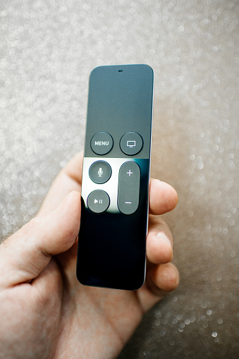 Paris, France - 25 Mar 2019: Directly above view of man hand holding modern Apple TV 4k player remote control with Siri assistant browsing Apple TV plus subscription film series documentaries