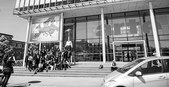 Strasbourg, France - May 23, 2019: Group of young funny black ethnicity childrens taking photo with the Homme Girafe statue in front of Arte Television headquarter - black and white image