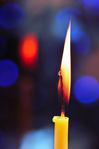 istock Closeup burning candle front of multi-colored lights 115485879