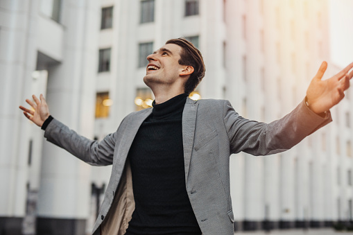 Close up of happy man smiling and raising his arms to the sky while going to or from work. Concept of happy employee or dissmissed, fired or going on vacation worker.