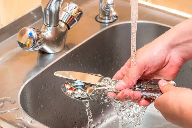hands close up - washing cutlery under running water in the kitchen