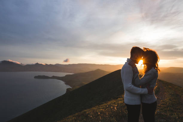 pareja feliz abrazando y besándose en la puesta de sol witn increíble vista de la montaña. cálida luz del sol por la noche - blowing men kissing blowing a kiss fotografías e imágenes de stock