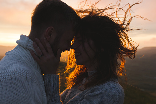 Gentle close-up portrait of man and woman together, happy, looking at each other. Silhouette at beautiful sunset light, wind in hair