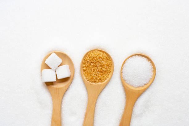 istock Wooden spoon with sugar on white granulated background 1154890471