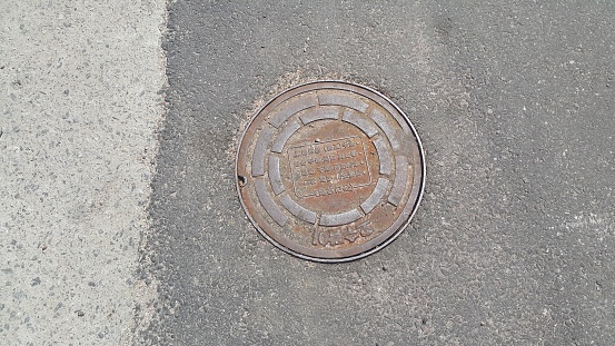Chuncheon, South Korea- May-2, 2019: Top view of a manhole cover on drainage or sewerage under paved road.