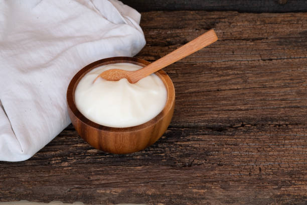 Natural homemade plain organic yogurt in wooden bowl and wood spoon on wood texture background, copy space
