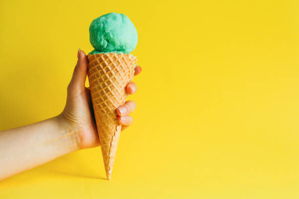 mano femenina sosteniendo helado cono helado aislado sobre un fondo amarillo vibrante - avocado portion fruit isolated fotografías e imágenes de stock