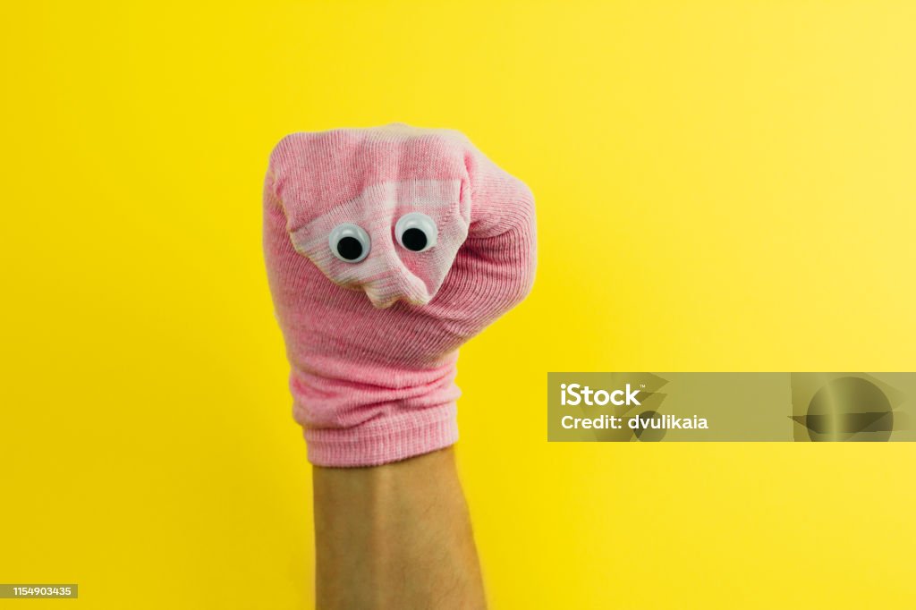funny doll  sock with googly eyes on a yellow background funny doll  sock with googly eyes on a yellow background, hand theater Bizarre Stock Photo