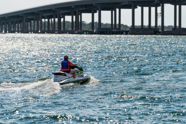 Woman skiing on jet ski outdoors at Gulf of Mexico ocean with view on US route 98 road bridge in Harborwalk Village, Florida Panhandle Destin, USA - April 24, 2018: Woman skiing on jet ski outdoors at Gulf of Mexico ocean with view on US route 98 road bridge in Harborwalk Village, Florida Panhandle harborwalk stock pictures, royalty-free photos & images