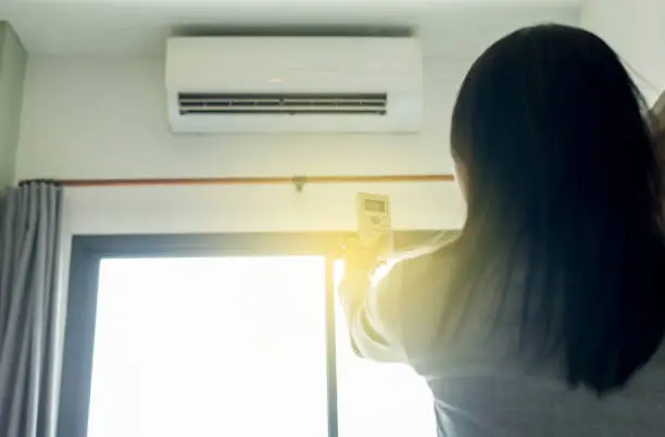 Photo of Woman hands using on a remote control to activating air conditioning system