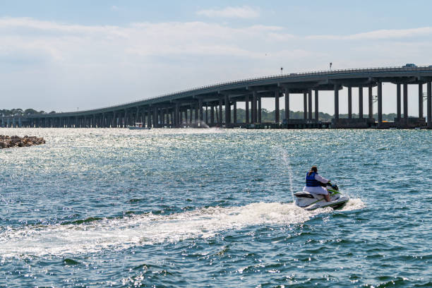 フロリダ州 harborwalk 村の米国路線98橋を眺めながら、メキシコ海湾の屋外でジェットスキーでスキーをする女性、パンハンドル - highway 99 ストックフォトと画像