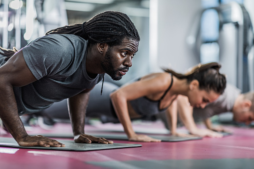 Sweaty black athletic man exercising push-ups with his friends in a gym.